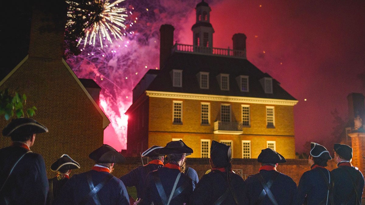 men in uniform looking towards building with fireworks in background for Fourth Of July Celebration at Colonial Williamsburg, Virginia, USA